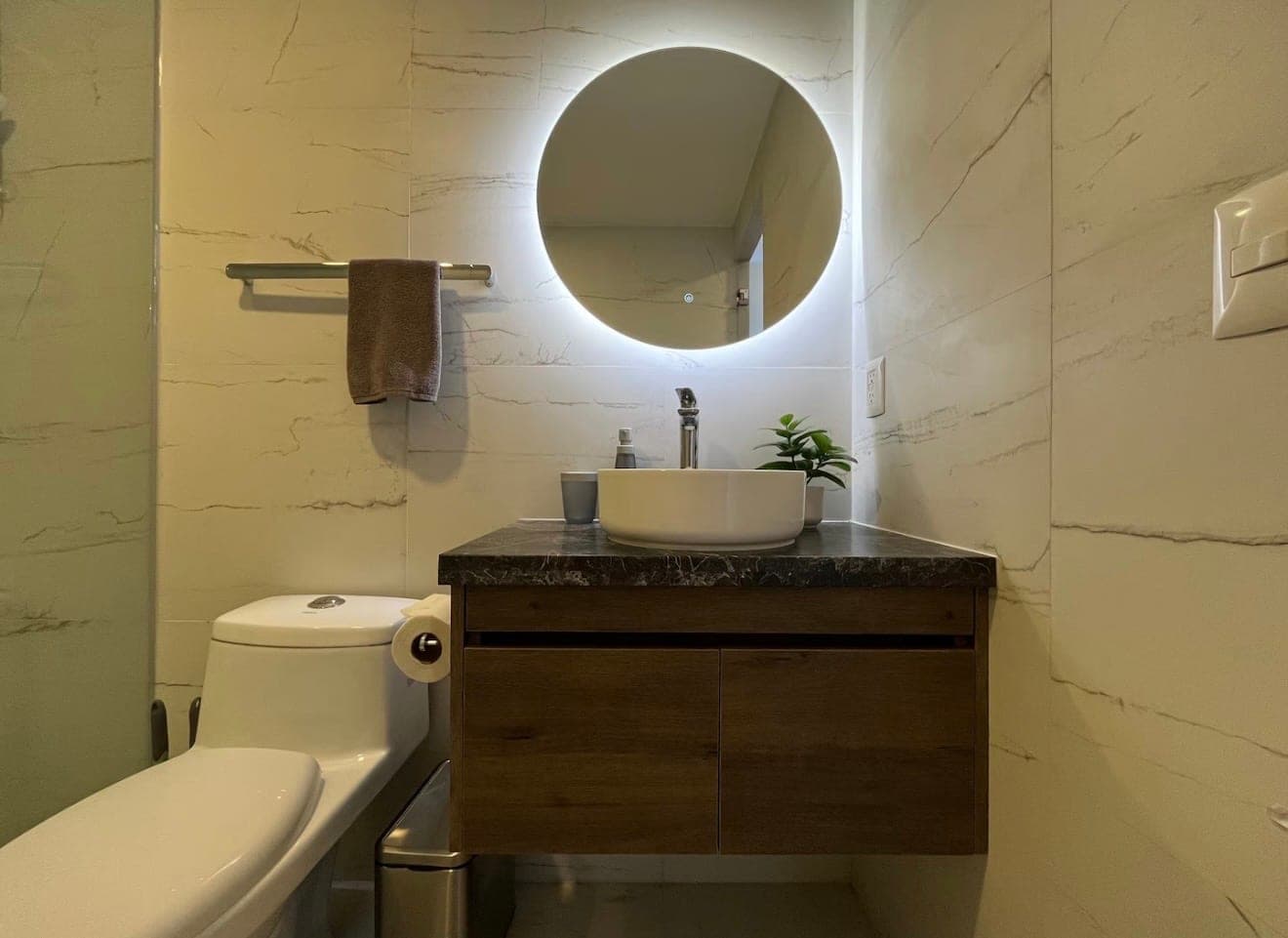 A clean bathroom with a lit round mirror, a vessel sink, and marble-look tile