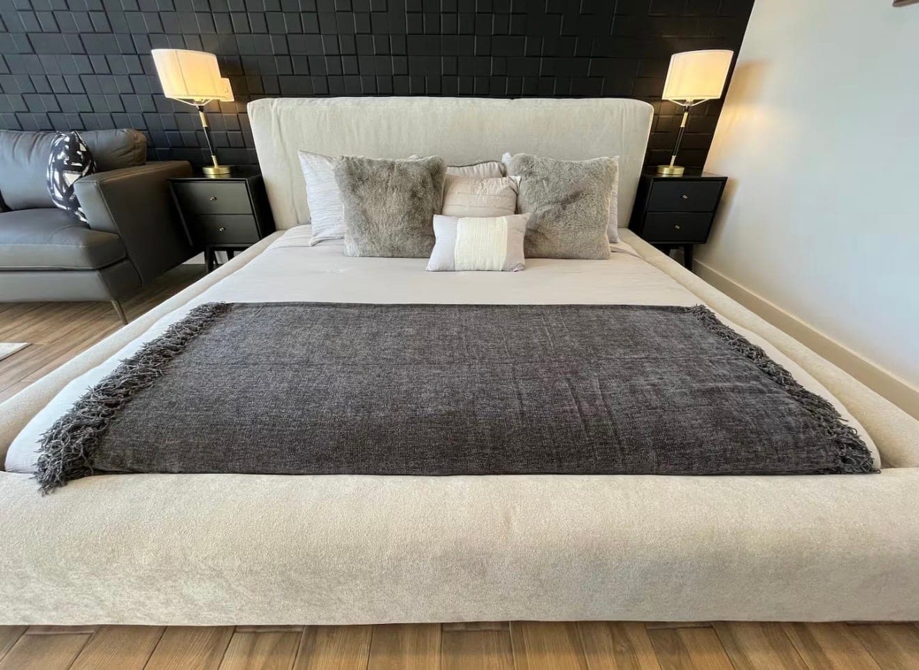 A neatly made bed with gray pillows in front of a black tiled accent wall