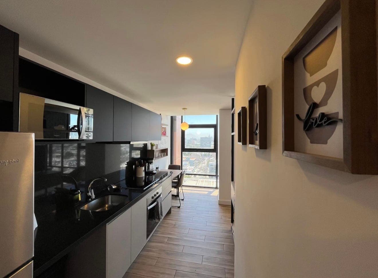 A spotless galley kitchen with black cabinets and a window looking out over the city
